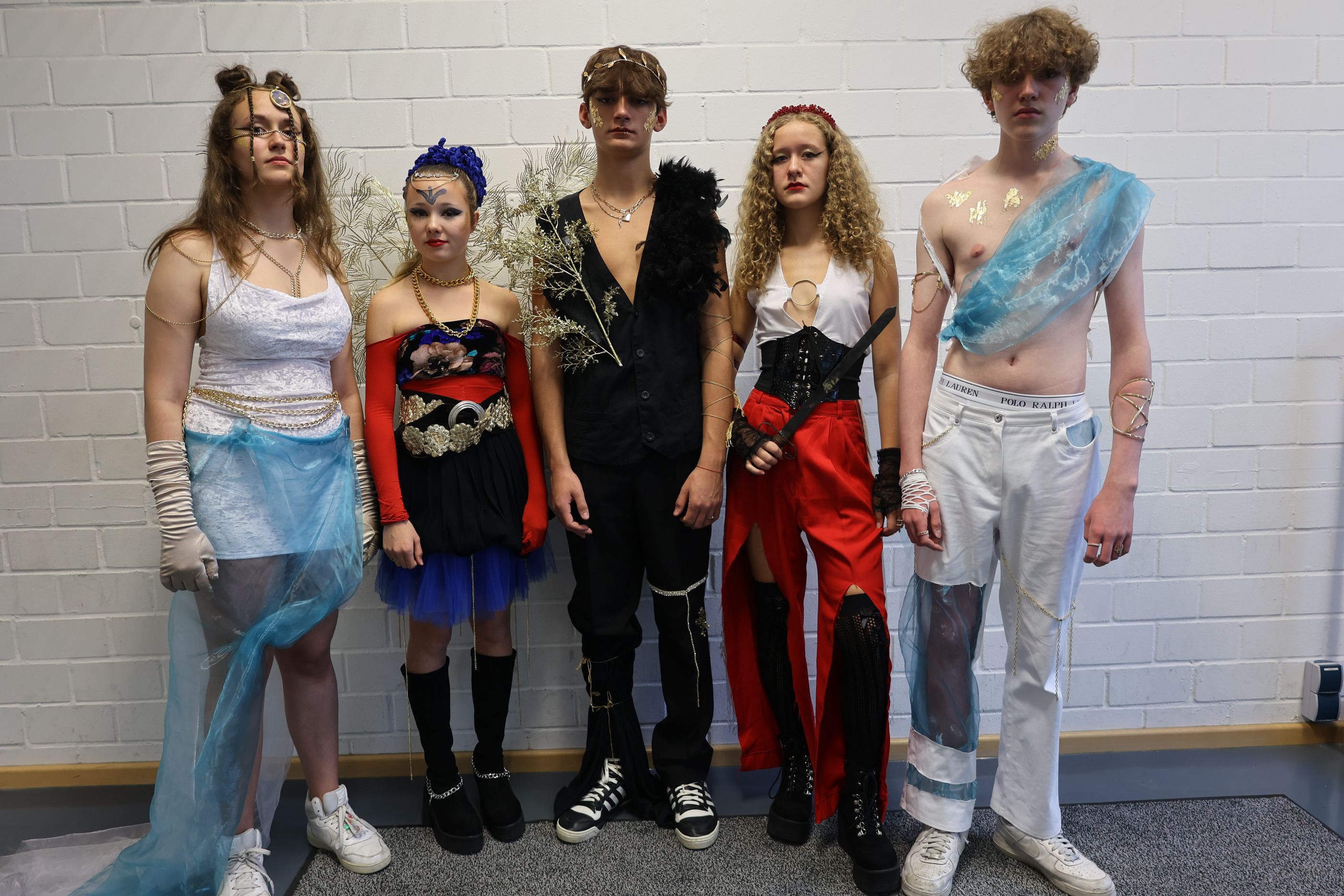 Fünf Models in den Looks der Kollektion nebeneinander vor einer weißen Backsteinwand.