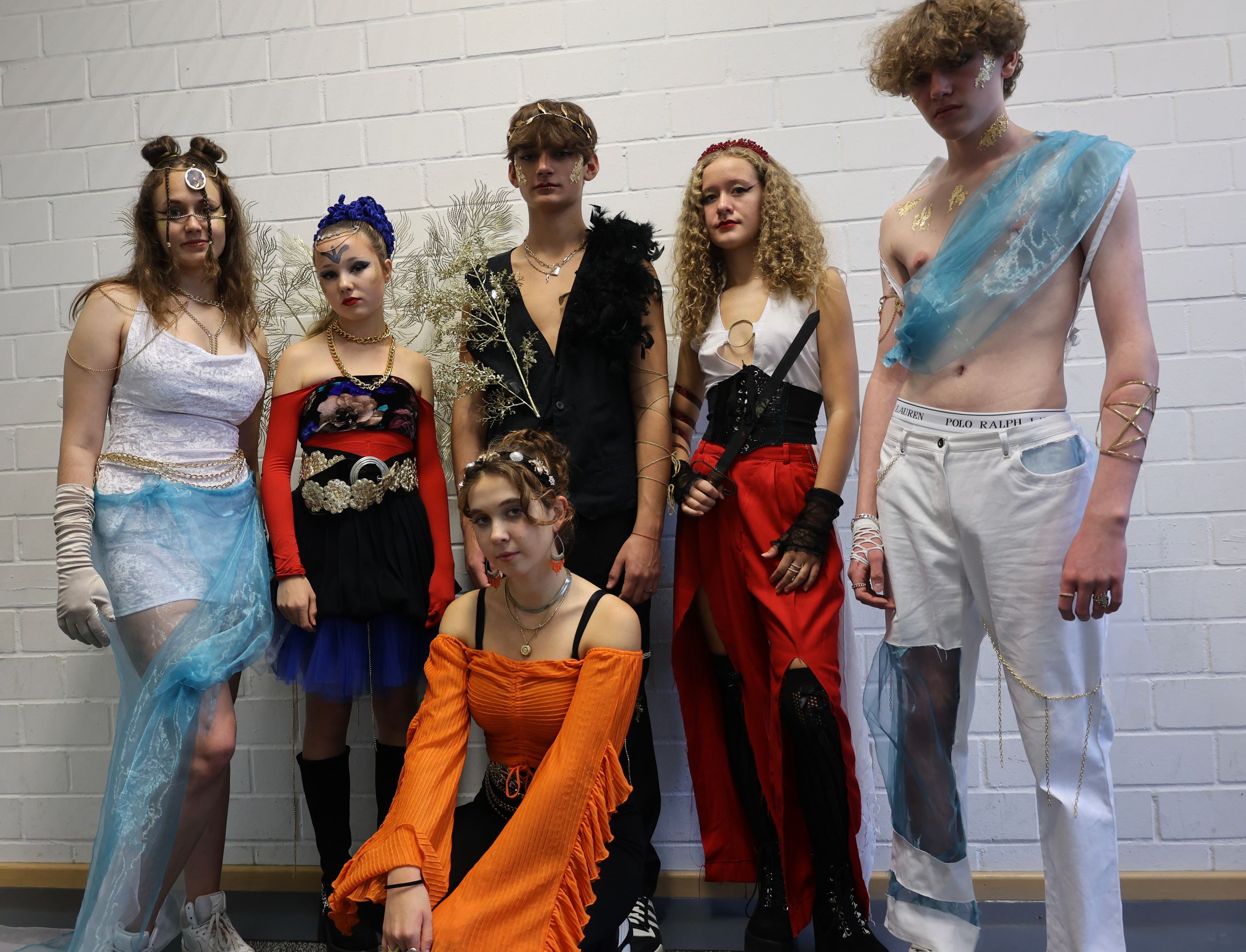 Gruppe von Models in selbst entworfenen Outfits vor einer weißen Backsteinwand.
