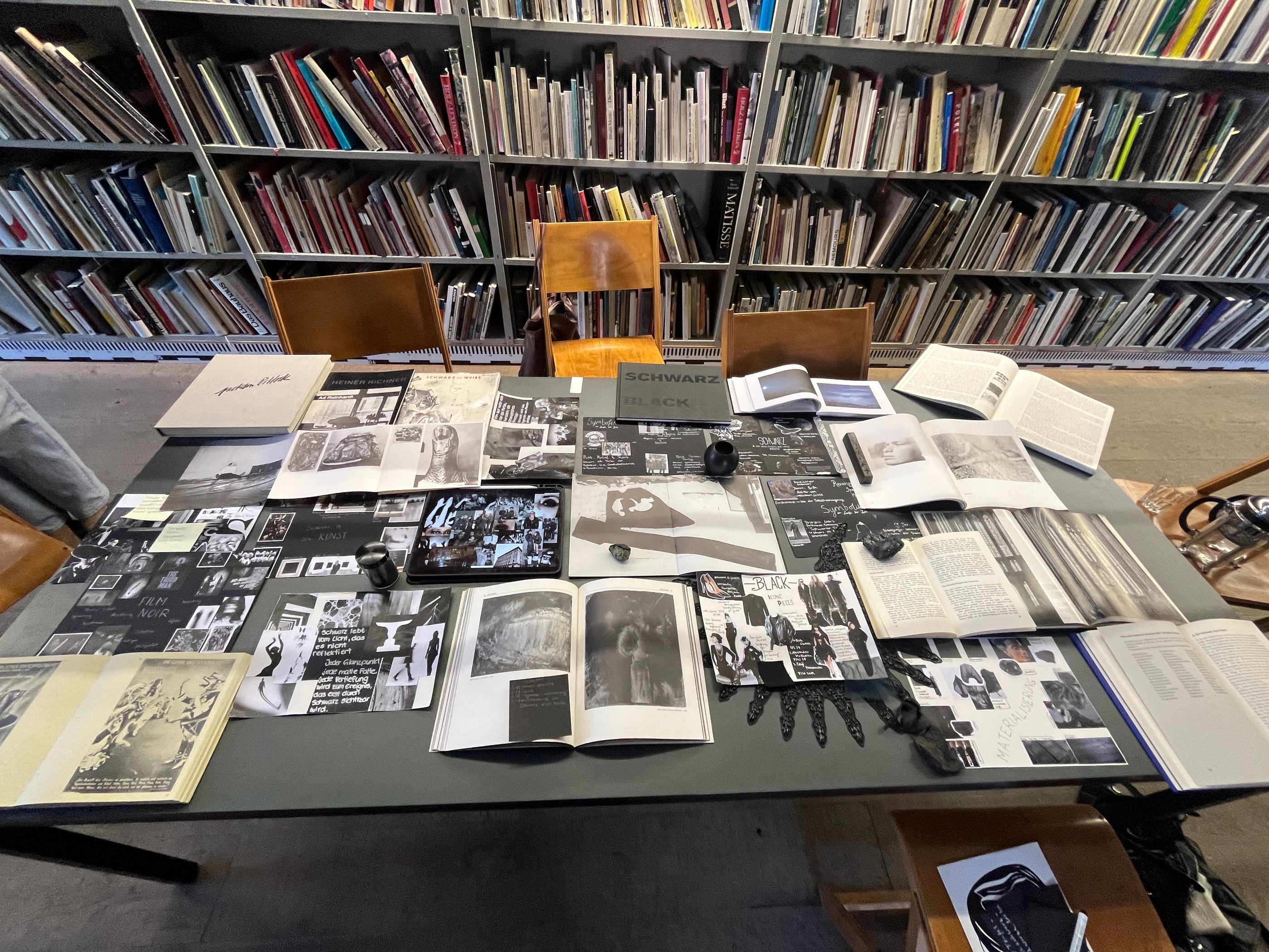 Arbeitstisch in einer Kunstbibliothek, bedeckt mit aufgeschlagenen Büchern und schwarzweißen Bildvorlagen.