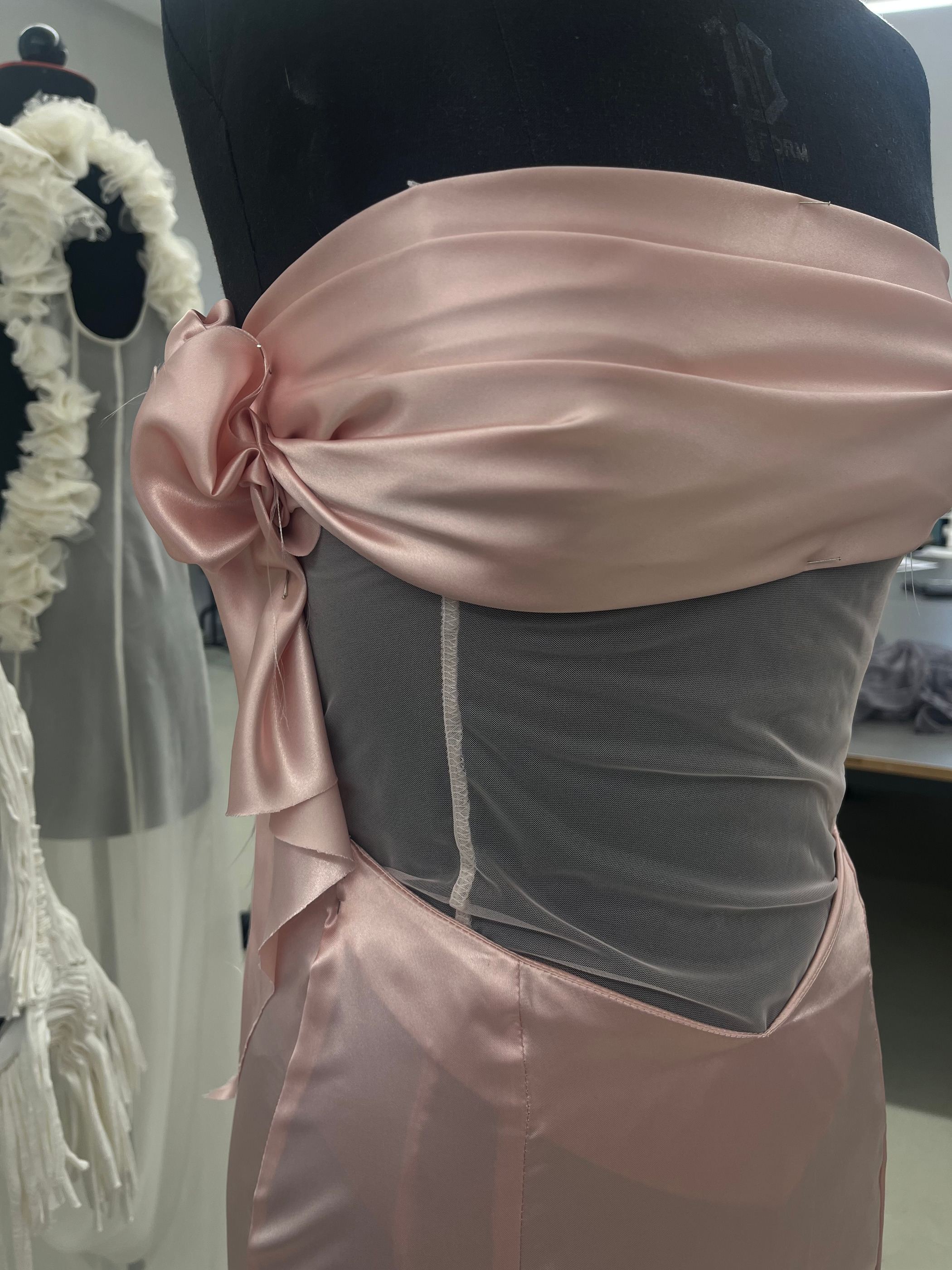 Detail am Kleiderständer: rosa Satinschärpe über transparentem Mesh.