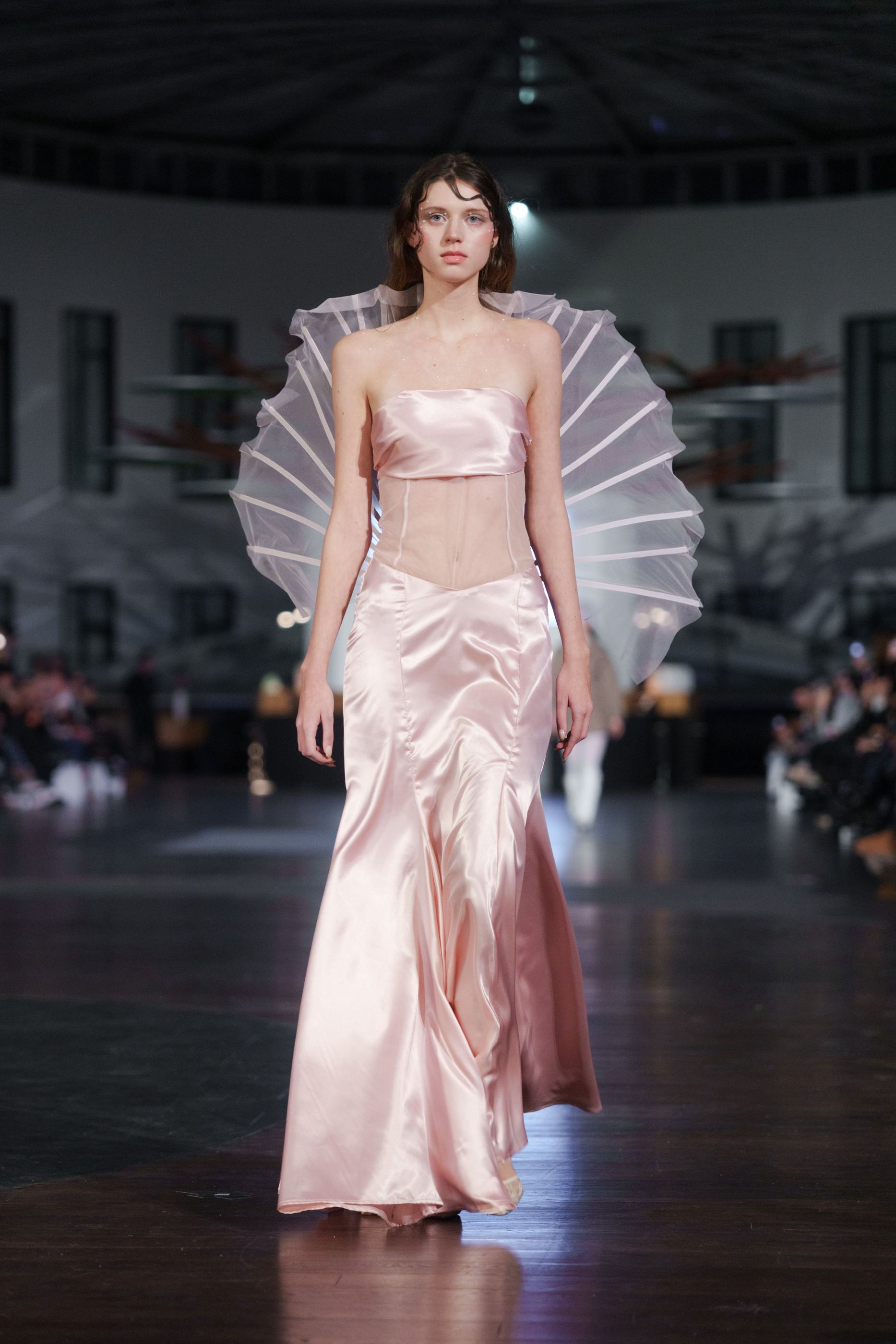 Model auf dem Laufsteg in bodenlanger rosa Satinrobe mit transparentem, fächerförmigem Rückenteil.