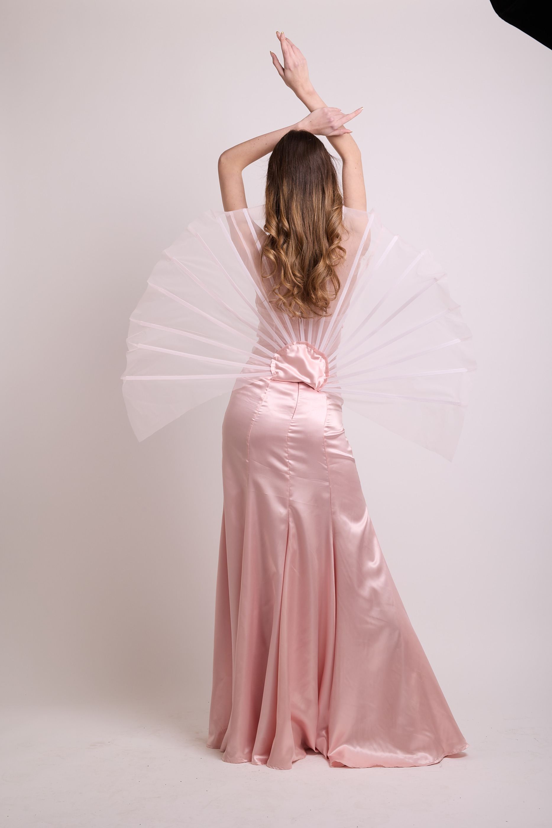 Rückansicht des Looks vor rosa Hintergrund, die Arme über dem Kopf, das gefächerte Rückenteil voll aufgespannt.