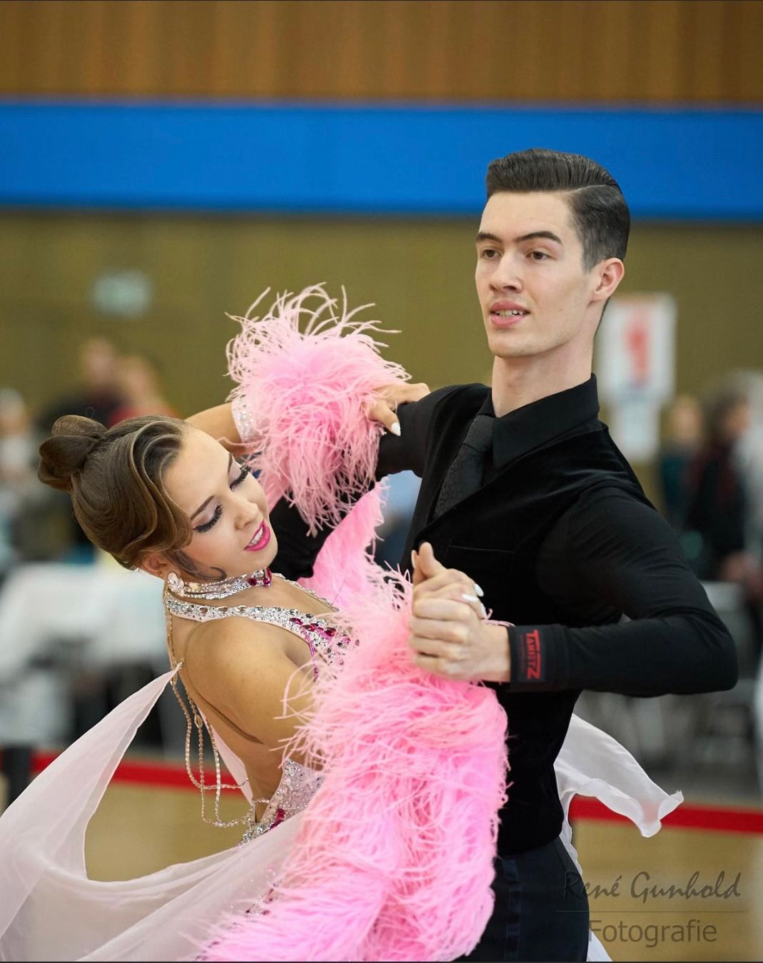 Ein Turniertanzpaar in Standardhaltung, das Kleid mit rosa Federbesatz.
