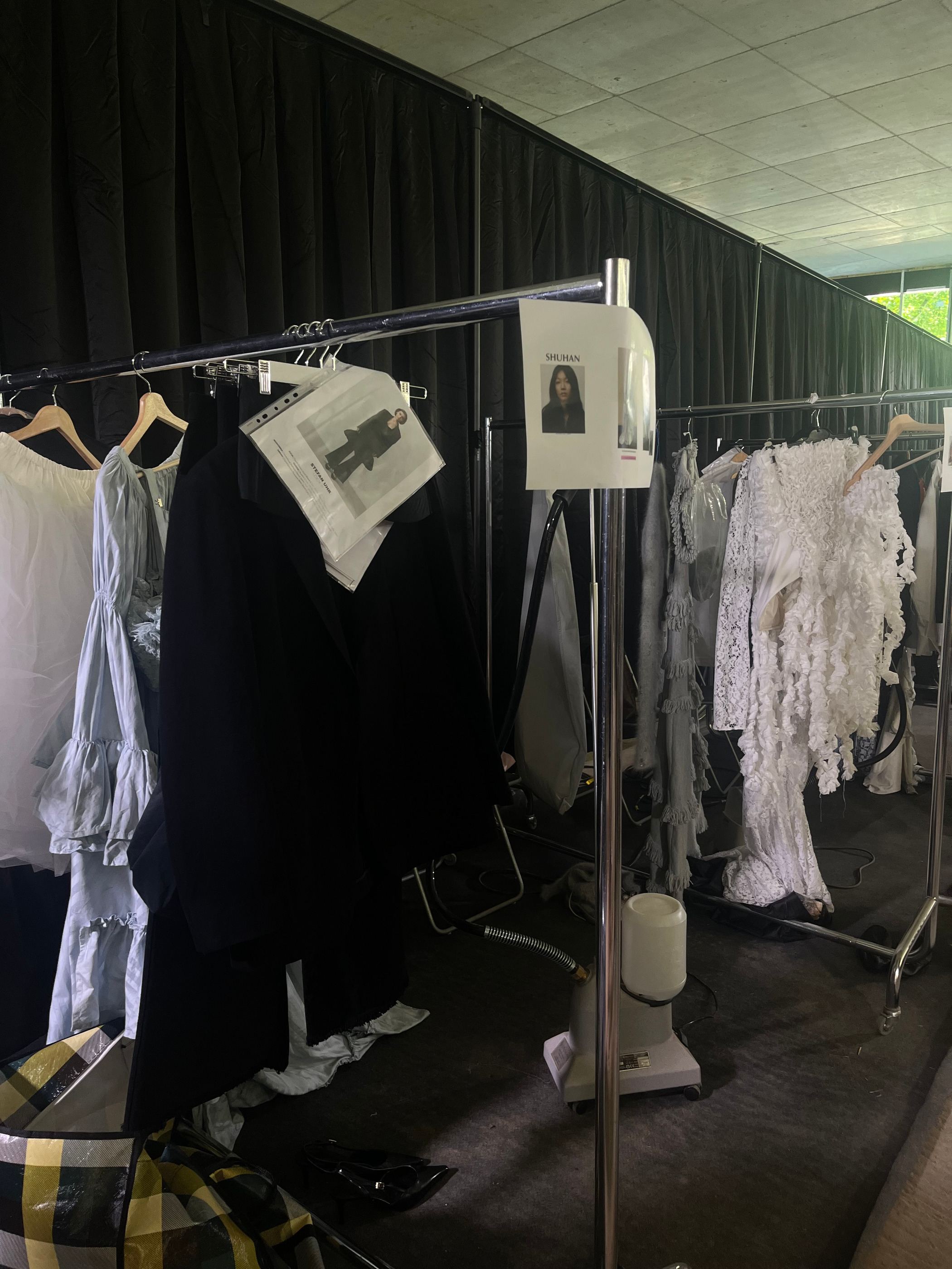 Zweite Kleiderstange mit hellen Looks, davor Arbeitsmaterial auf dem Boden.