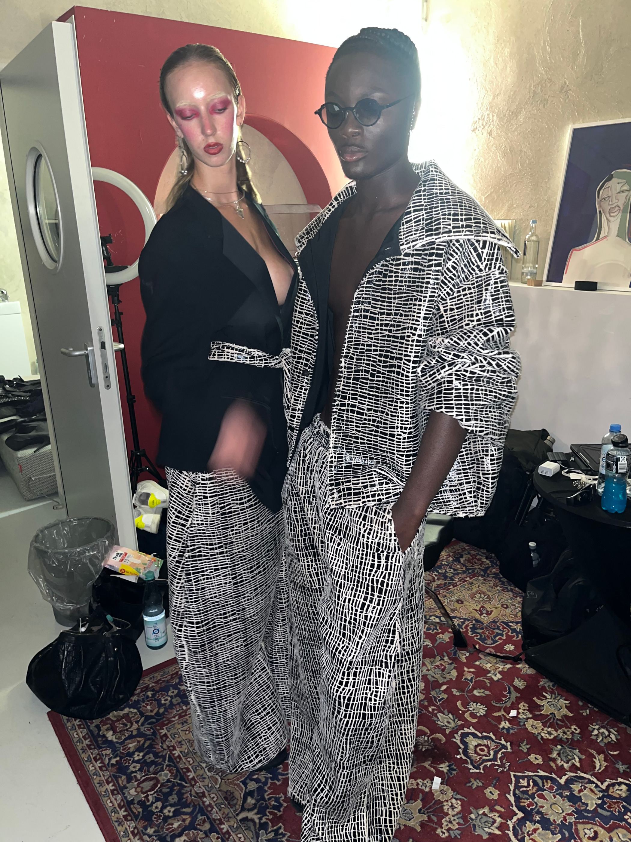 Zwei Models in schwarzen und gemusterten Looks im Ankleidebereich.